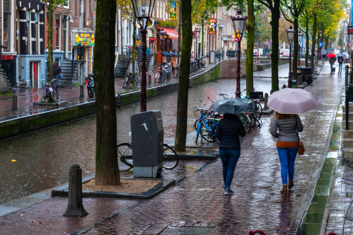 Two-woman-with-umbrellas-walking-along-a-raony-canal-street-in-Amsterdam