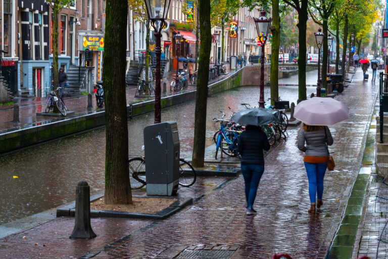 Two-woman-with-umbrellas-walking-along-a-rainy-canal-street-in-Amsterdam