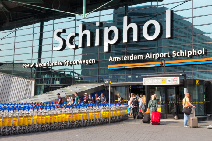 Facade-of-Schiphol-airport-with-man-pushing-long-line-of-baggage-carriages