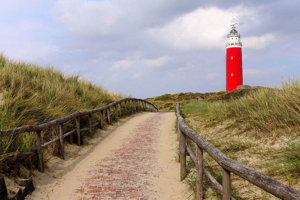 Scenic-path-in-dunes-of-Texel-with-red-lighthouse-and-wooden-fences