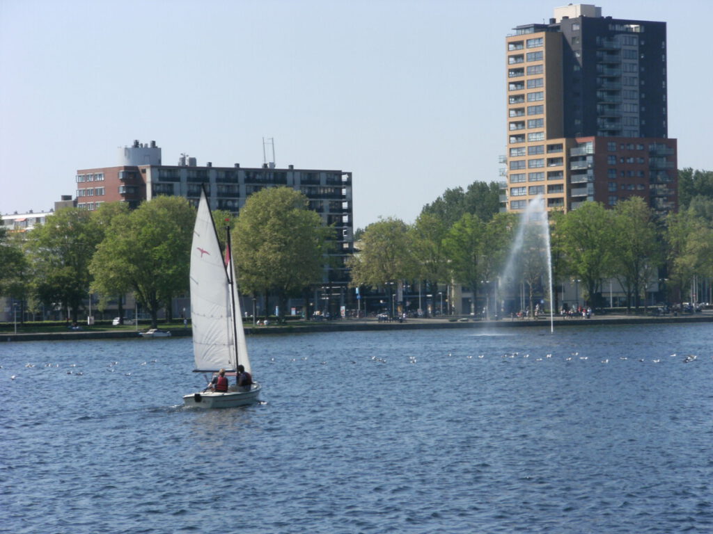 sloterplas lake in amsterdam with sail boat on the water and buildings in the back and a water fountain