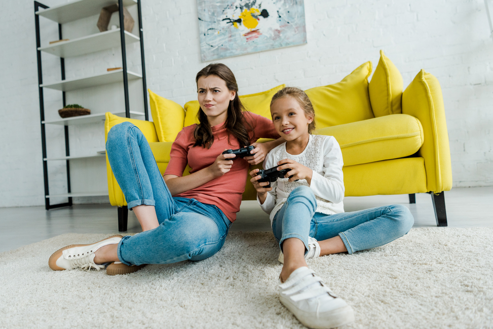 Woman-next-to-young-girl-sitting-in-front-of-couch-playing-video-game