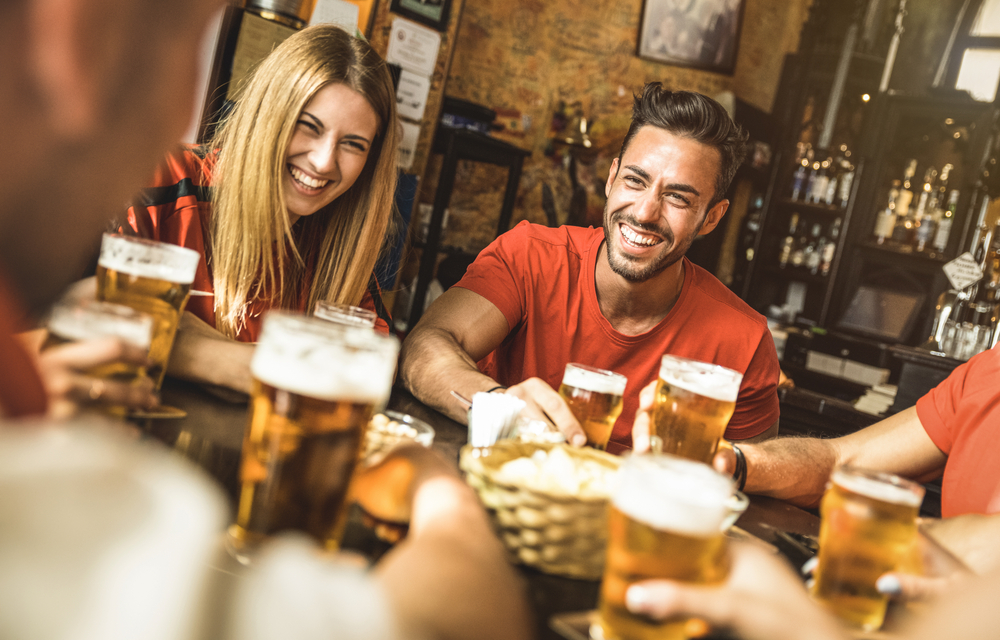 Group-of-friends-sitting-around-a-table-smiling-with-pints-of-beer