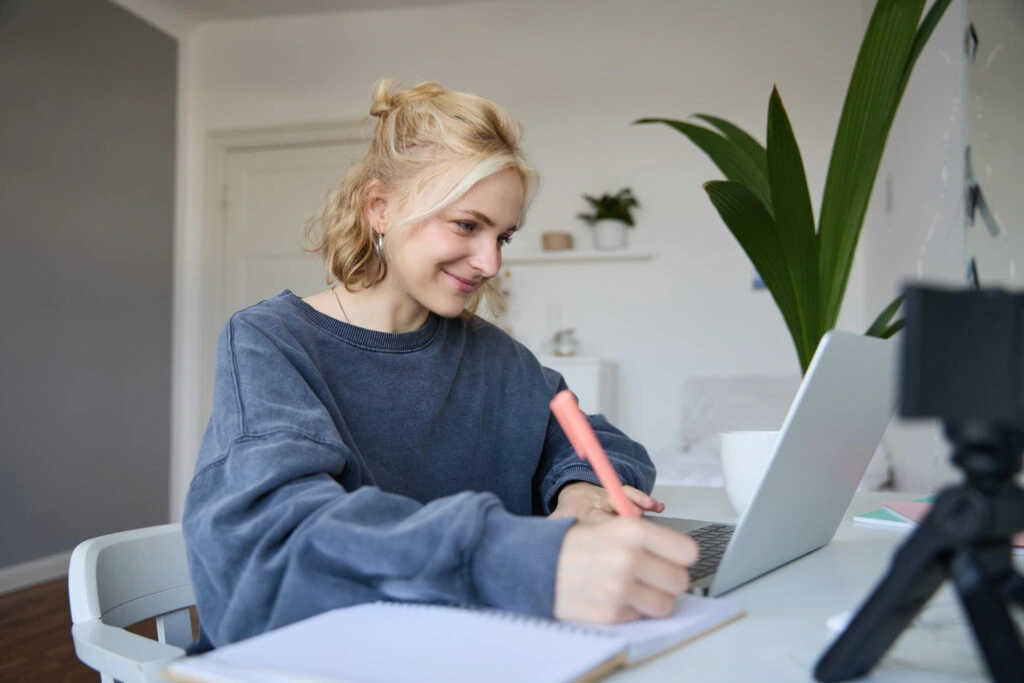 woman-taking-online-Dutch-course-with-taalthuis-sitting-at-laptop-taking-notes-and-smiling