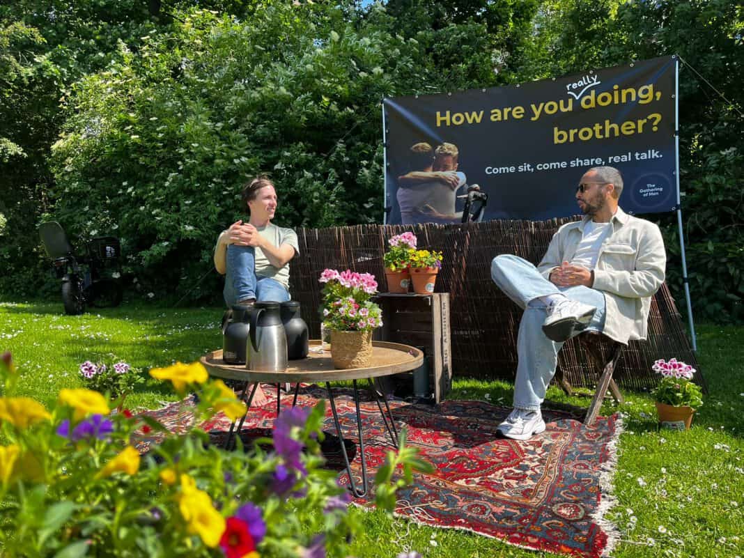 picture-of-two-men-sitting-on-chair-in-a-park-setting-surrounded-by-flowers-chatting