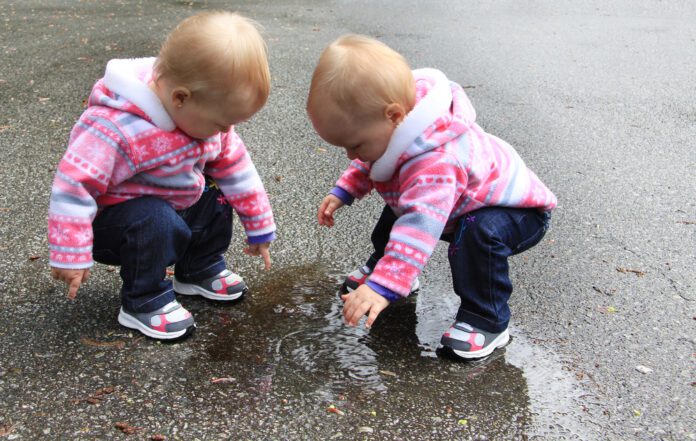 Twin-baby-girls-in-pink-coats-playing-in-puddle-of-water