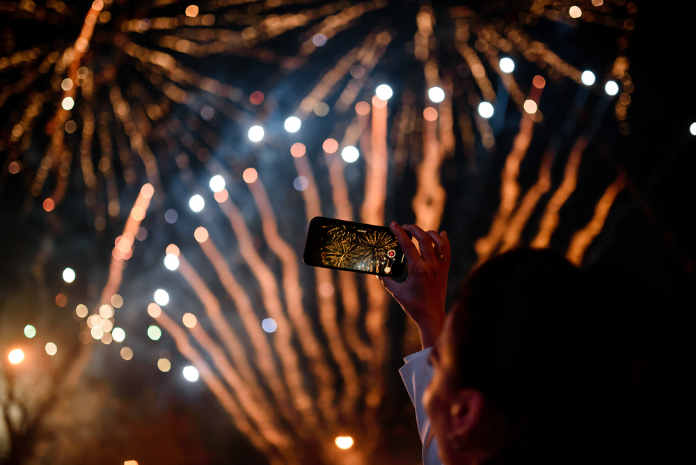 woman-taking-a-picture-on-her-phone-of-red-and-orange-firworks-in-the-dark