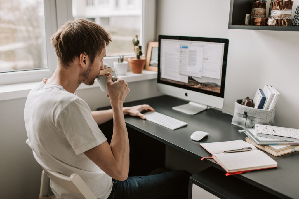 Man-working-from-home-on-desk-top-computer-and-drinking-coffee