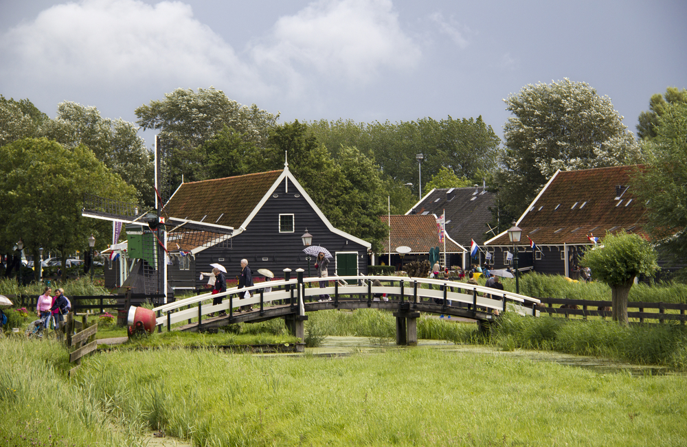 People-walking-over-bridge-Dutch-houses-windmill-at-beautiful-Zaanse-Schans-Netherlands
