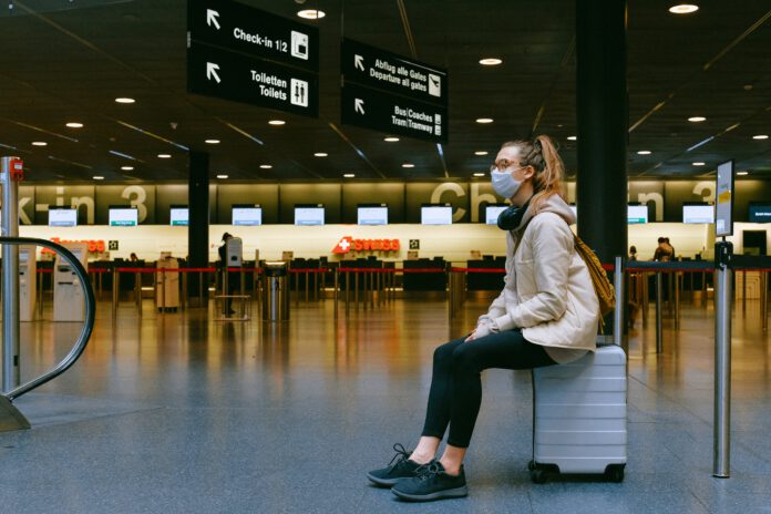 Woman-wearing-a-mask-sitting-on-her-luggage-case-at-the-airport