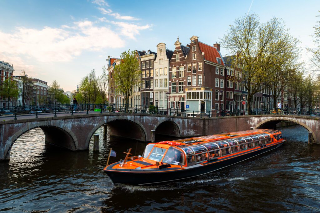 photo-of-amsterdam-canal-tourist-boat-near-bridge-with-canal-houses-in-background