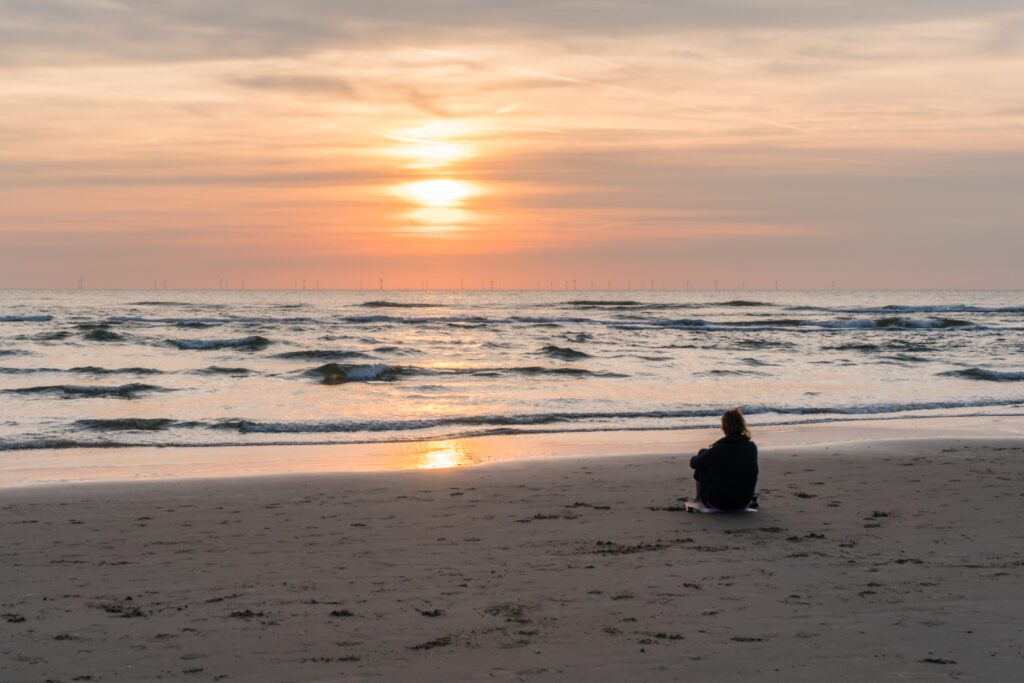 Egmond-aan-Zee, one of the best beaches in the Netherlands. There is a girl sitting in the sand at the seafront during sunset
