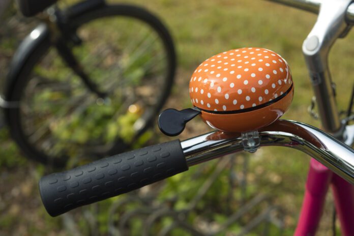 orange-and-white-polka-dotted-bike-bell-on-handle-bar-close-up-against-grass-and-bike-wheel