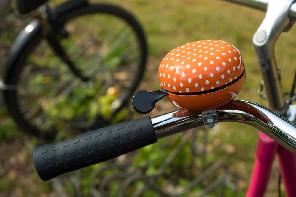 orange-and-white-polka-dotted-bike-bell-on-handle-bar-close-up-against-grass-and-bike-wheel-for-riding-a-bicycle-in-the-netherlands