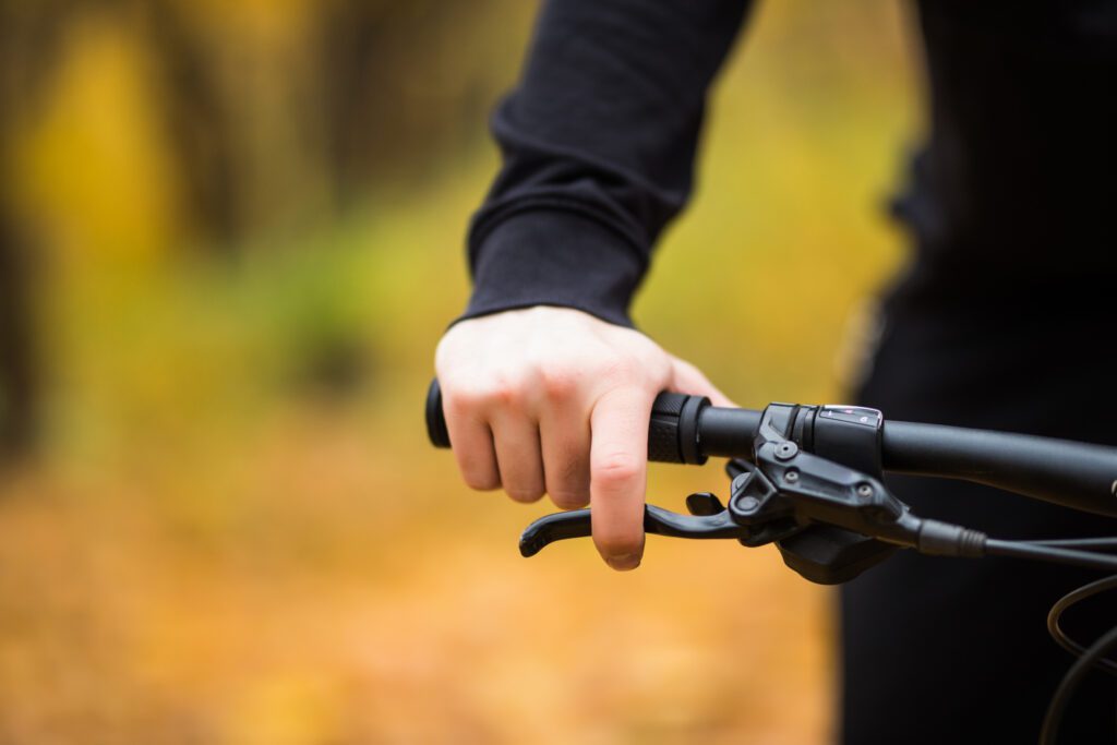 bikers-hand-on-handlebars-while-riding-through-autumn-park-close-up-scaled