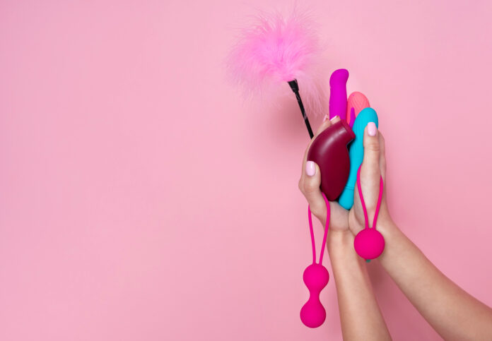 Close-up-shot-of-hands-holding-different-sex-toys-with-pink-background