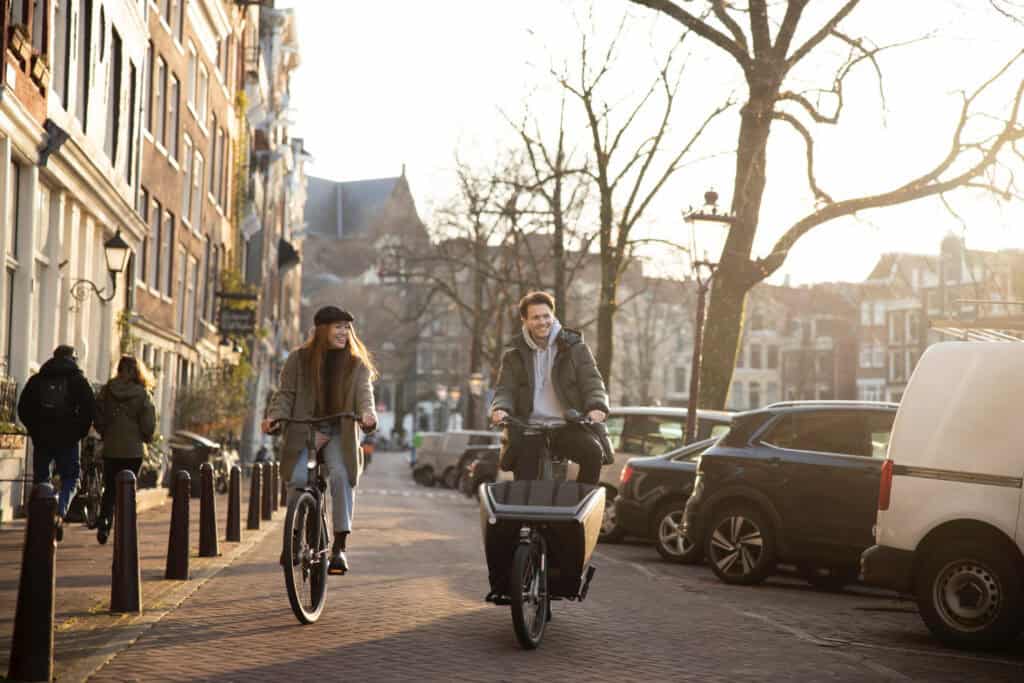 photo-of-man-and-woman-cycling-on-amsterdam-street-in-cold-weather-and-sun