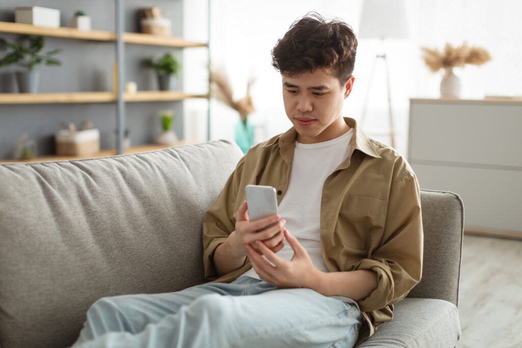 depressed-man-talking-to-family-on-phone-expat-in-the-netherlands-sitting-on-couch-holding-smartphone