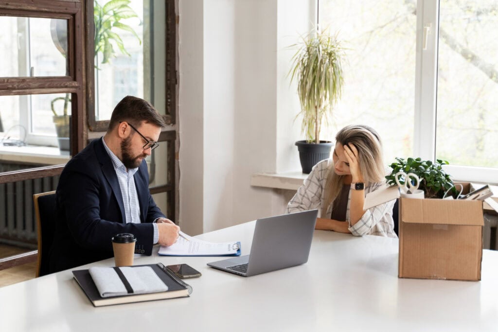 photo-of-woman-and-boss-sitting-at-desk-while-woman-gets-made-redundant-from-her-job-in-the-Netherlands