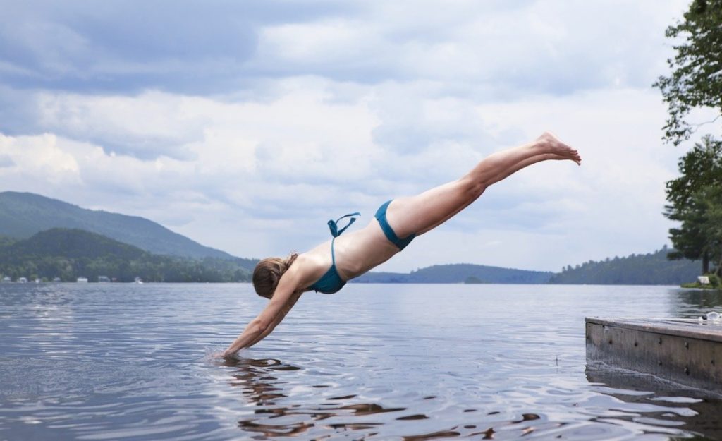 Woman-in-a-blue-bikini-diving-head-first-into-a-lake-with-mountains-in-the-background
