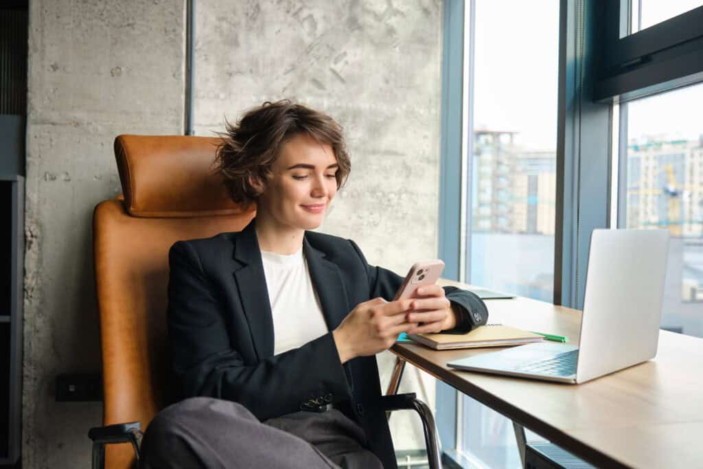 dutch-freelancer-checking-her-cashback-on-the-finom-mobile-phone-app-with-open-laptop-in-front-of-her