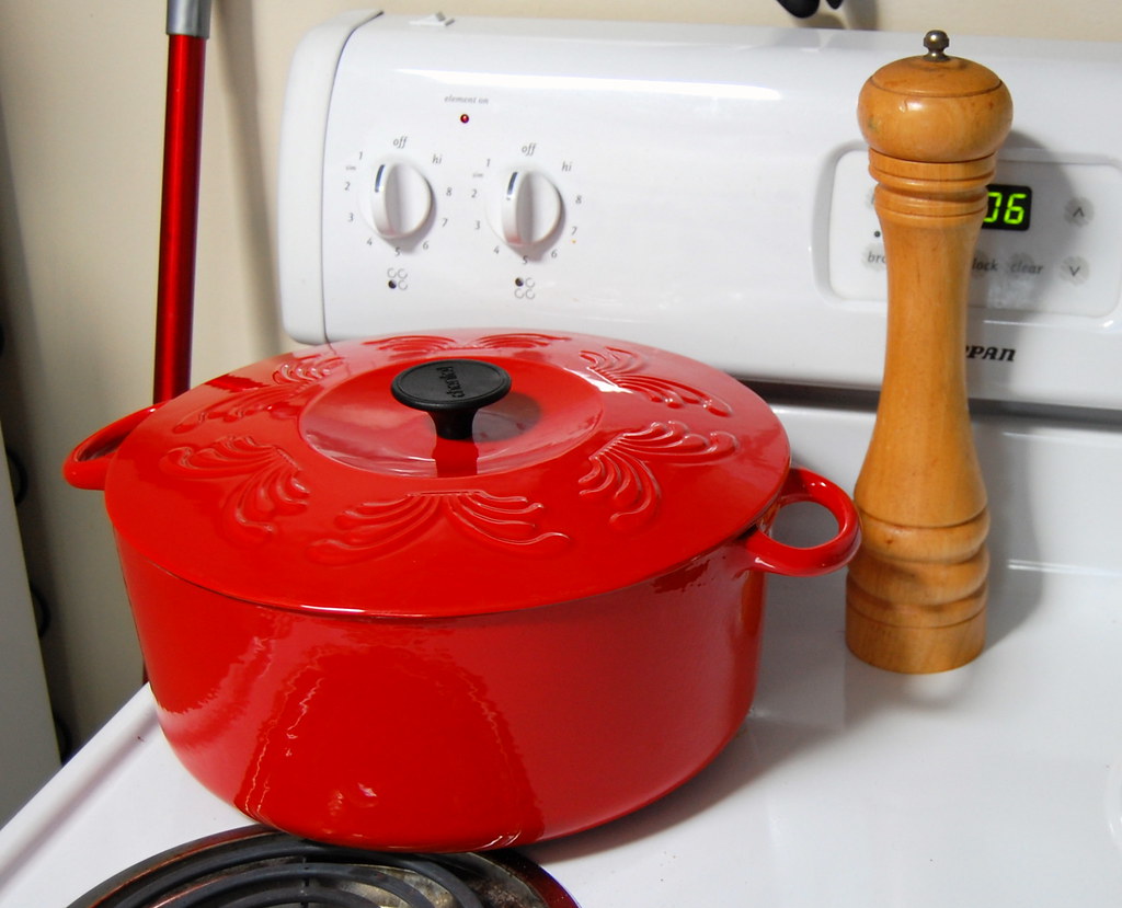 Image-of-a-red-dutch-oven-pott-standing-on-a-white-stove-next-to-pepper-grinder