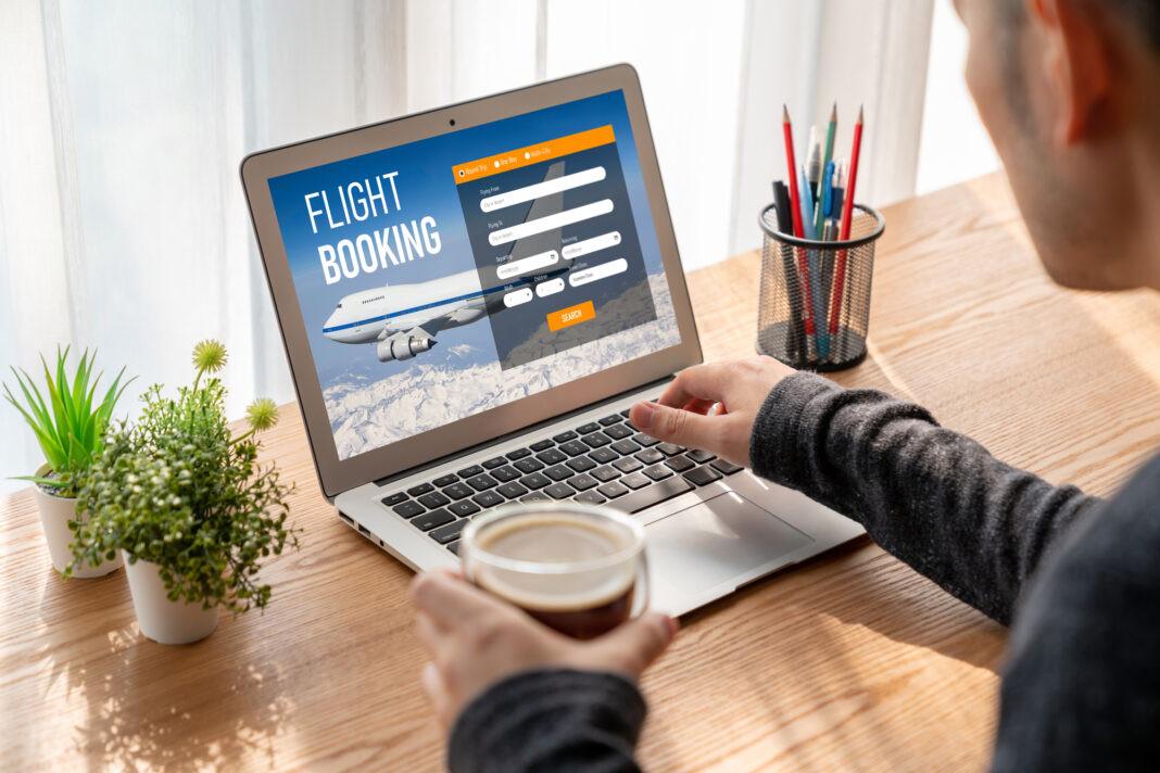 photo-of-man-booking-flights-on-laptop-holding-coffee