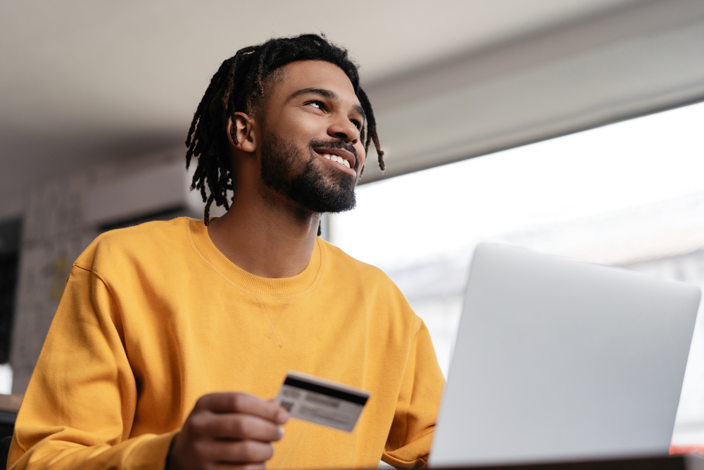 photo-young-man-holding-bank-card-receiving-international-money-transfer-from-laptop