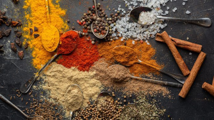 a-mix-of-different-coloured-spices-with-spoons-poured-out-on-black-table