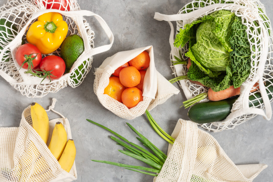 Fresh vegetables and fruits in tote eco friendly bags on grey table top view.
