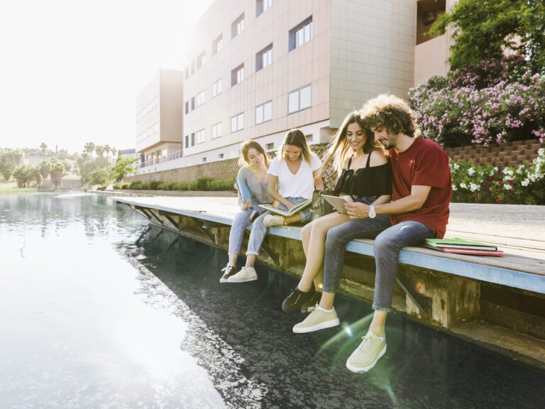 student-friends-smiling-and-studying-near-building-with-legs-dangling-over-lake-while-setting-up-things-after-moving-to-the-Netherlands-to-study