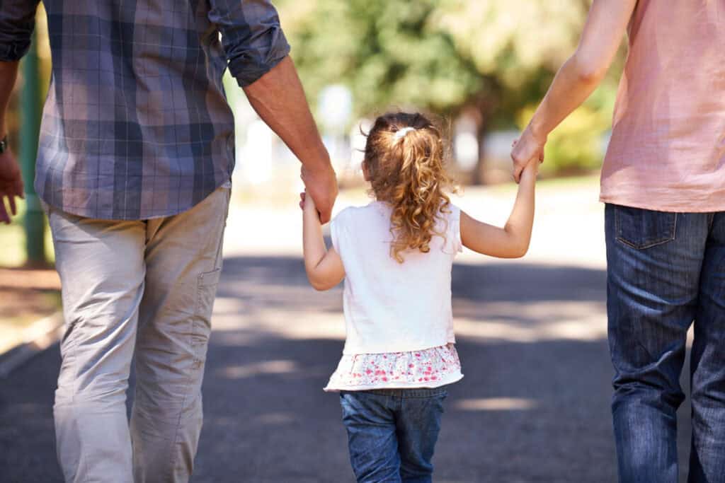 photo-of-back-of-little-girl-holding-hands-with-her-parents-as-they-walk-down-road