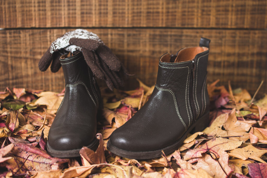 photo-of-gloves-lying-on-top-of-a-pair-of-thick-winter-boots-on-a-bed-of-red-orange-yellow-autumn-leaves