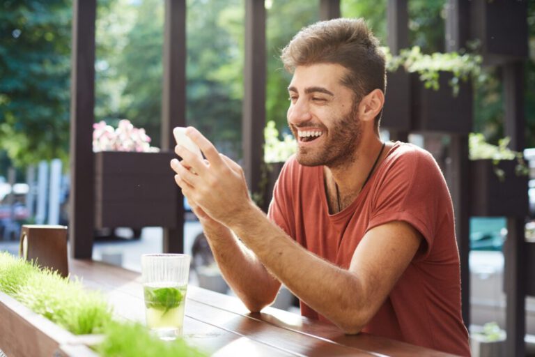 photo-of-happy-man-using-phone-in-green-cafe-getting-cashback-from-his-bank