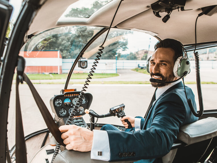 helicopter-interior-cabin-man-with-beard-in-suit-steering-controls-turning-to-look-over-left-shoulder-while-smiling