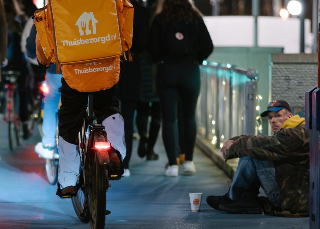 photo-of-homeless-man-sitting-on-bridge-in-amsterdam-as-people-bicycle-past