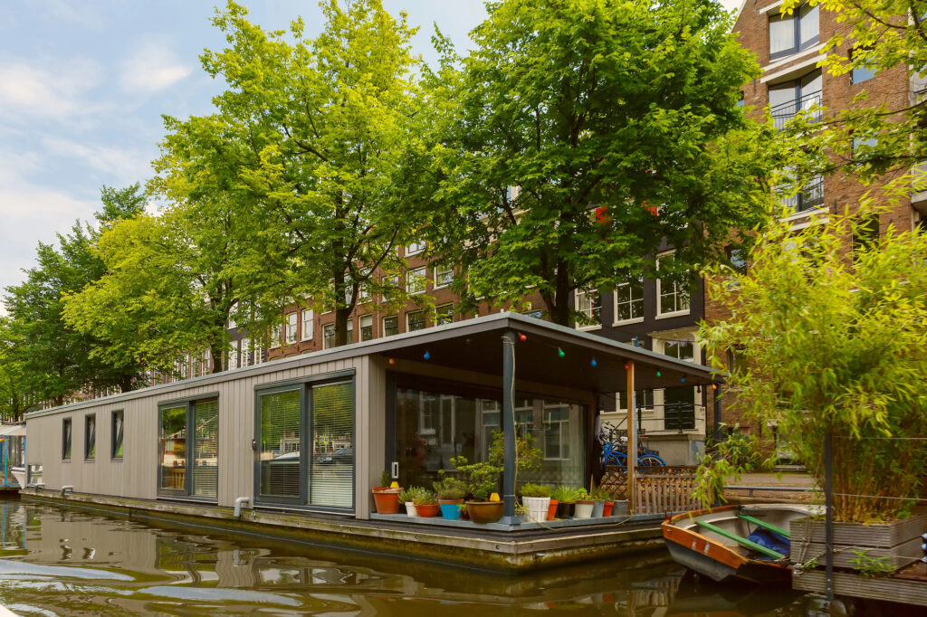 house-boat-docked-in-Amsterdam-canal-on-street-lined-with-lush-trees