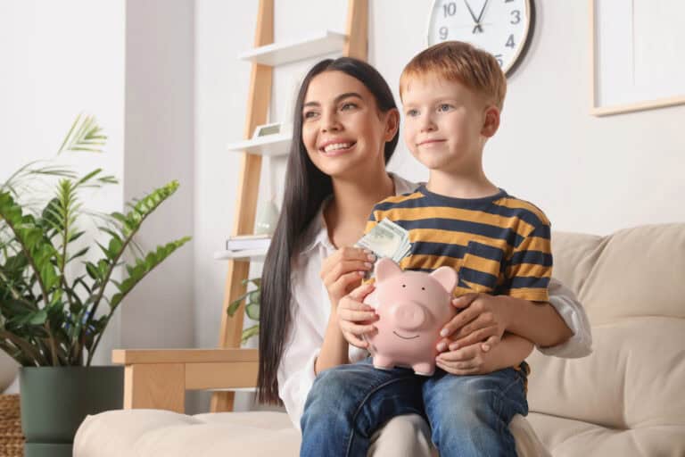 Mother with money and her son holding piggy bank at home saving for a house deposit in the Netherlands