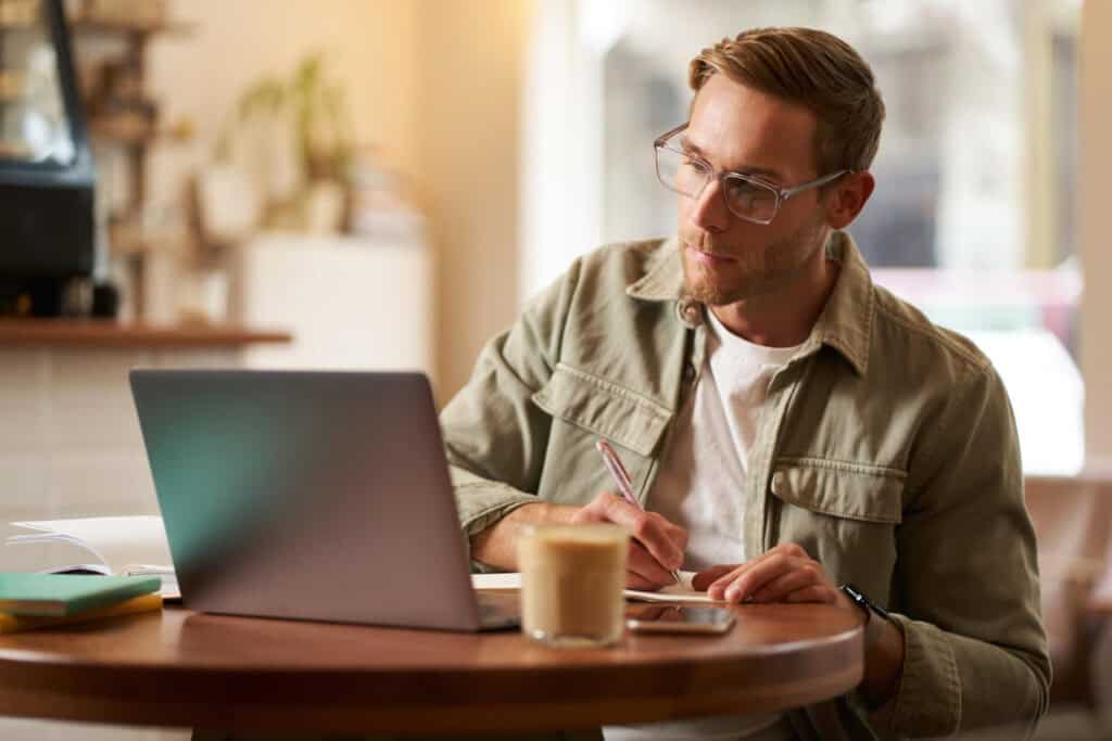 photo-of-man-looking-up-how-much-he-has-to-earn-to-buy-a-house-in-the-Netherlands-on-laptop-with-cup-of-coffee