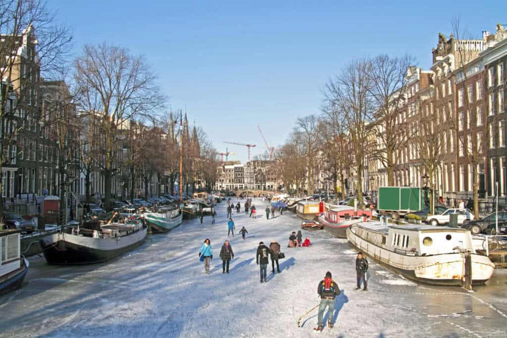 photo-of-sunny-day-in-amsterdam-people-ice-skating-on-frozen-canal-during-winter