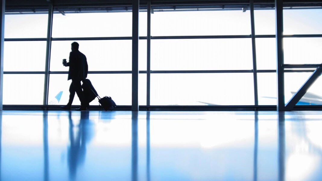 photo-of-silhoutted-man-in-airport-against-bright-windows-walking-with-suitcase