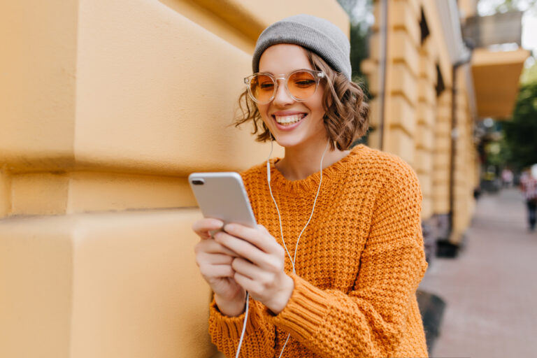 international-in-orange-jumper-listening-to-music-via-earbuds-with-mobile-that-has-simyo-esim-connection