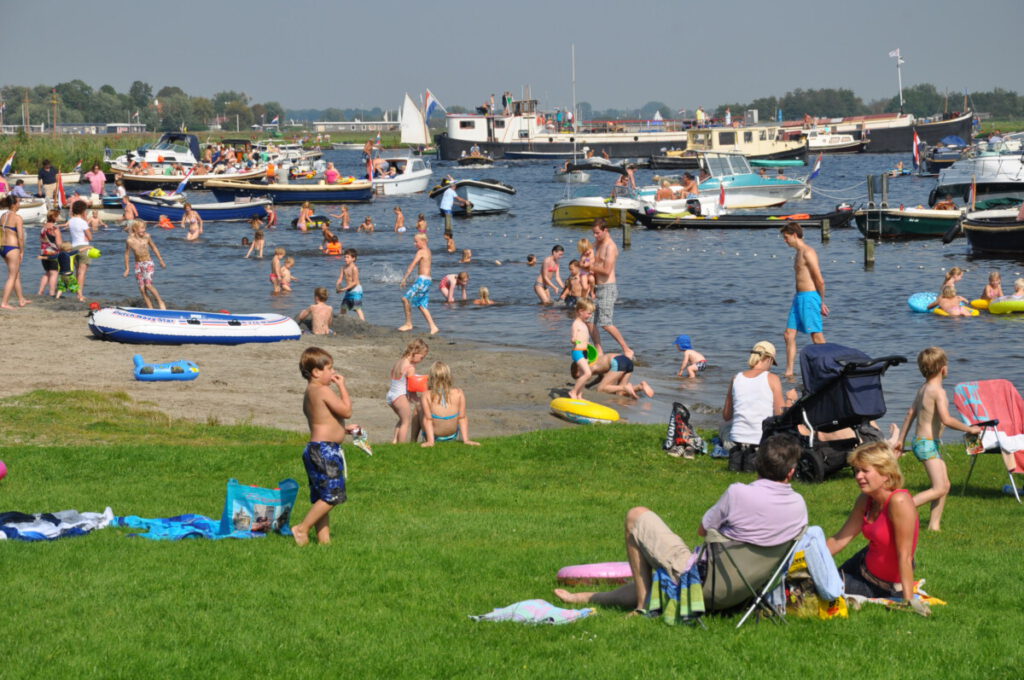 families-with-children-lounging-on-beach-at-harbour-with-boats-in-the-distance