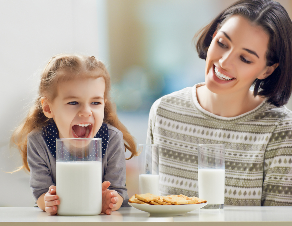 photo-of-little-girl-sitting-with-mom-drinking-huge-glass-of-milk-with-cookies
