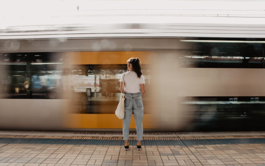 young-woman-standing-at-platform-looking-at-yellow-amsterdam-london-train-go-past