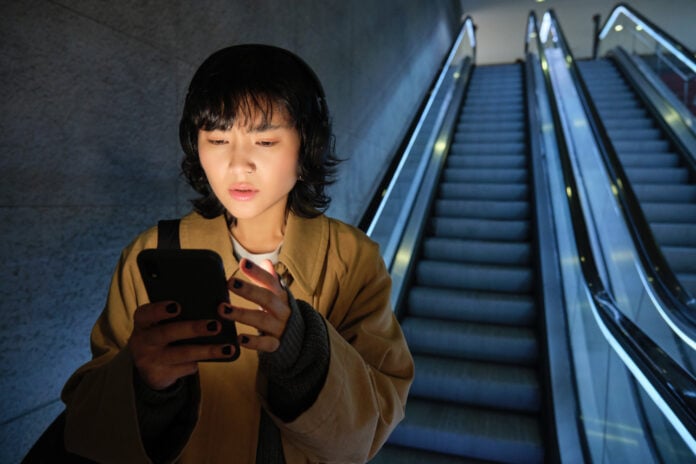 photo-of-asian-woman-looking-at-phone-while-travelling-down-escalator