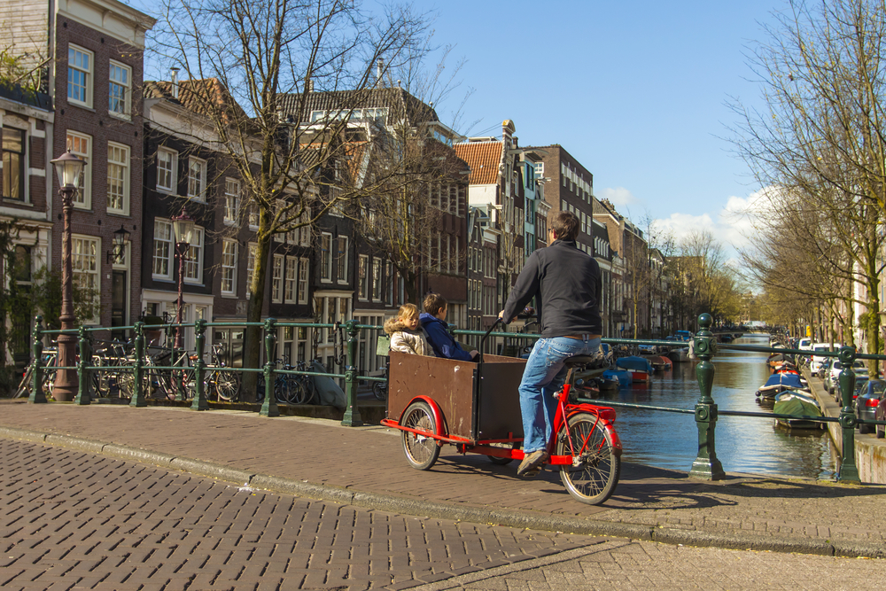 father-biking-in-amsterdam-bakfiets-with-two-kids