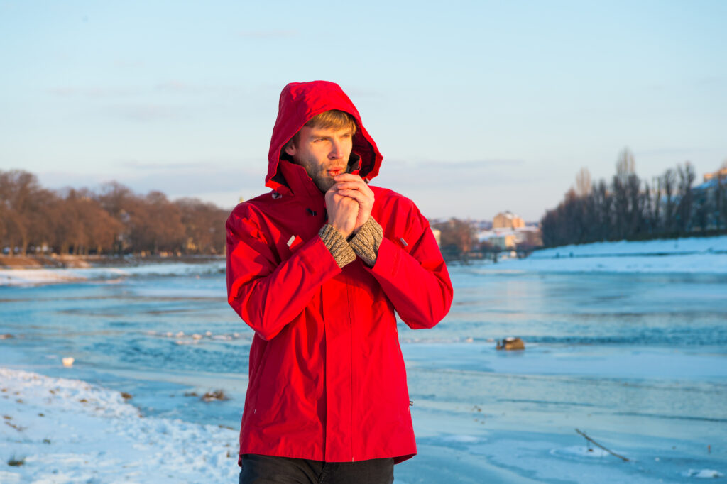 photo-of-dutch-man-dressed-in-a-red-parka-standing-by-a-lake-and-looking-cold-blond-hair-blue-frozen-background