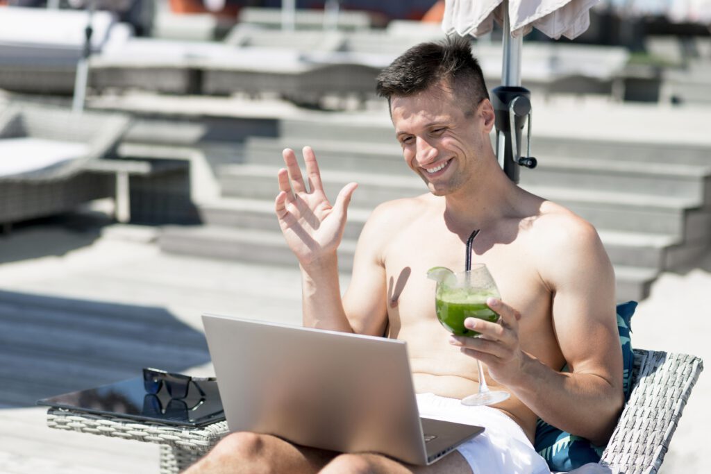 man-sitting-by-a-pool-with-a-drink-in-his-hand-and-using-his-work-laptop