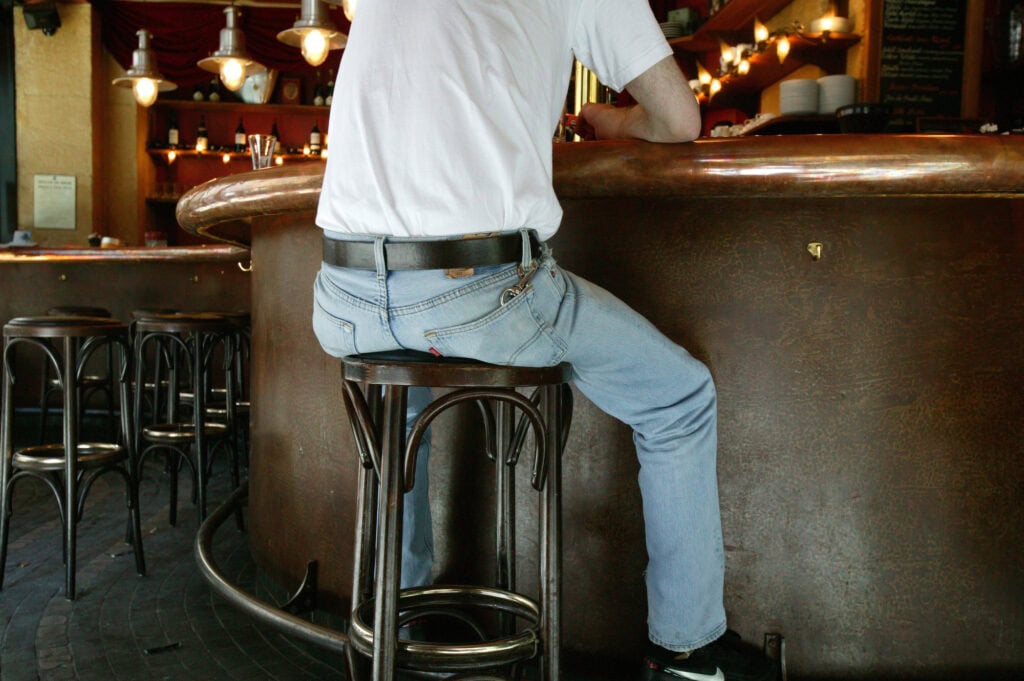 photo-of-a-man-casually-dressed-sitting-on-a-bar-stool-back-to-the-camera-in-a-bar